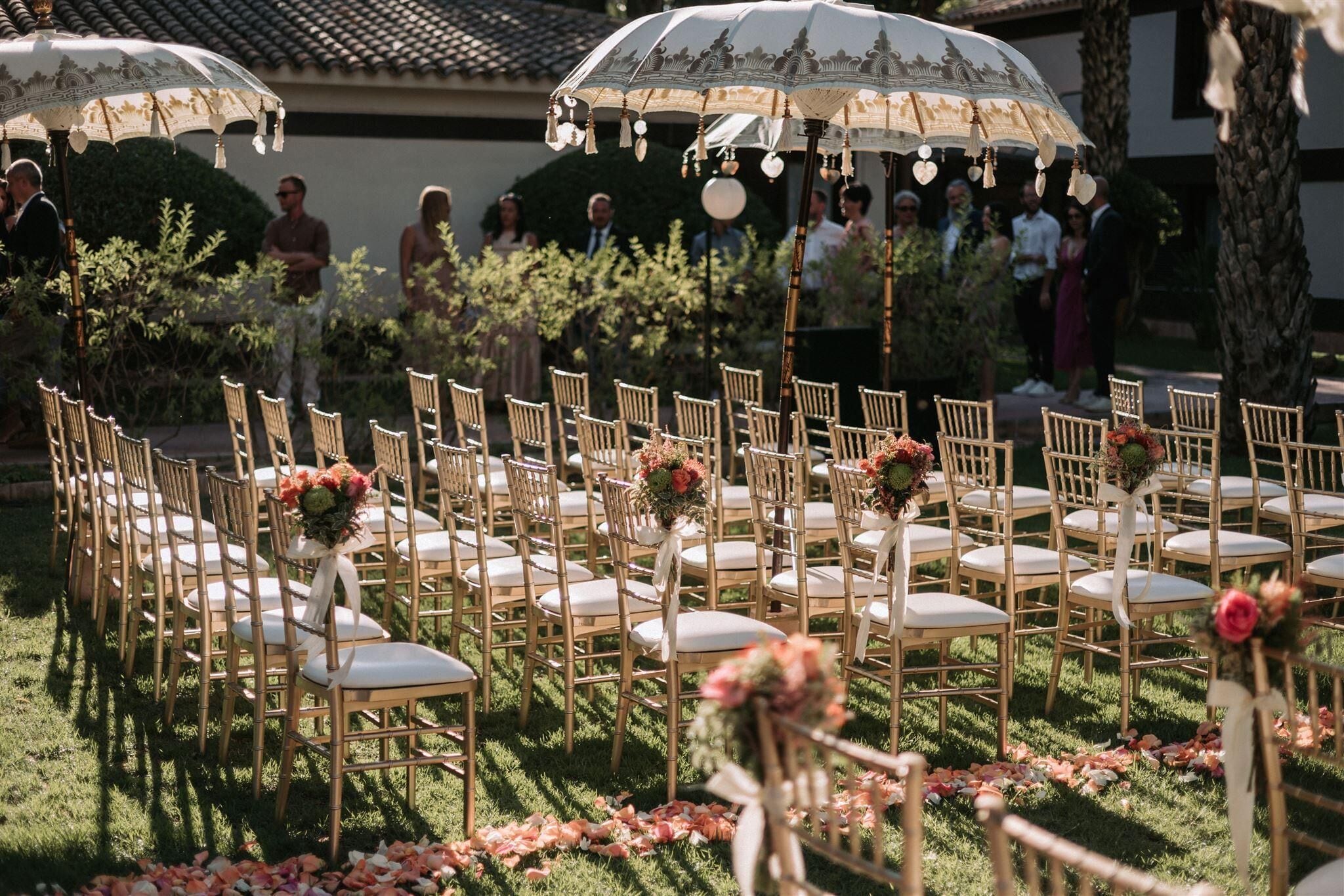 Location per matrimonio all'aperto con file di sedie di legno e cuscini bianchi disposti a semicerchio.