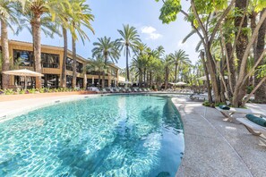 A swimming pool with clear water, surrounded by palm trees and lounge chairs.