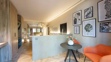 Un vestíbulo de hotel moderno con un mostrador de recepción de madera, una mesa redonda con un jarrón de flores e impresiones botánicas enmarcadas en la pared.