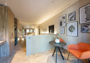 Un hall d’hôtel moderne avec un comptoir d’accueil en bois, une table ronde ornée d’un vase de fleurs et des reproductions encadrées de gravures botaniques accrochées au mur.