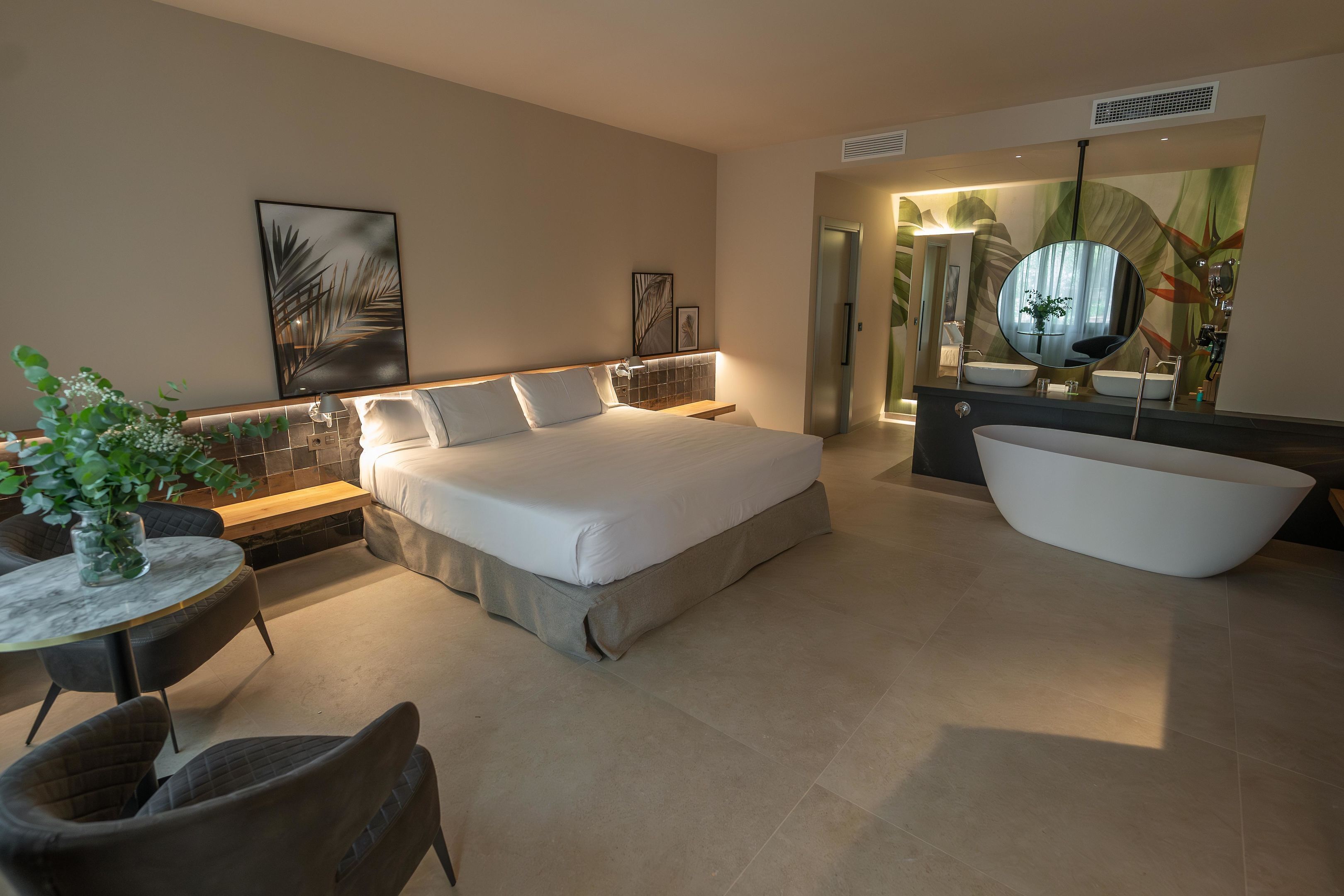 Ein modernes Hotelzimmer mit einem großen Bett, einer Sitzecke mit Tisch und Stühlen, einer Badewanne und Kunstwerken an den Wänden.