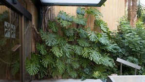 A modern building with a glass entrance, a concrete floor, and a wooden wall with large green plants. - Huerto Del Cura Hotel (Elche)