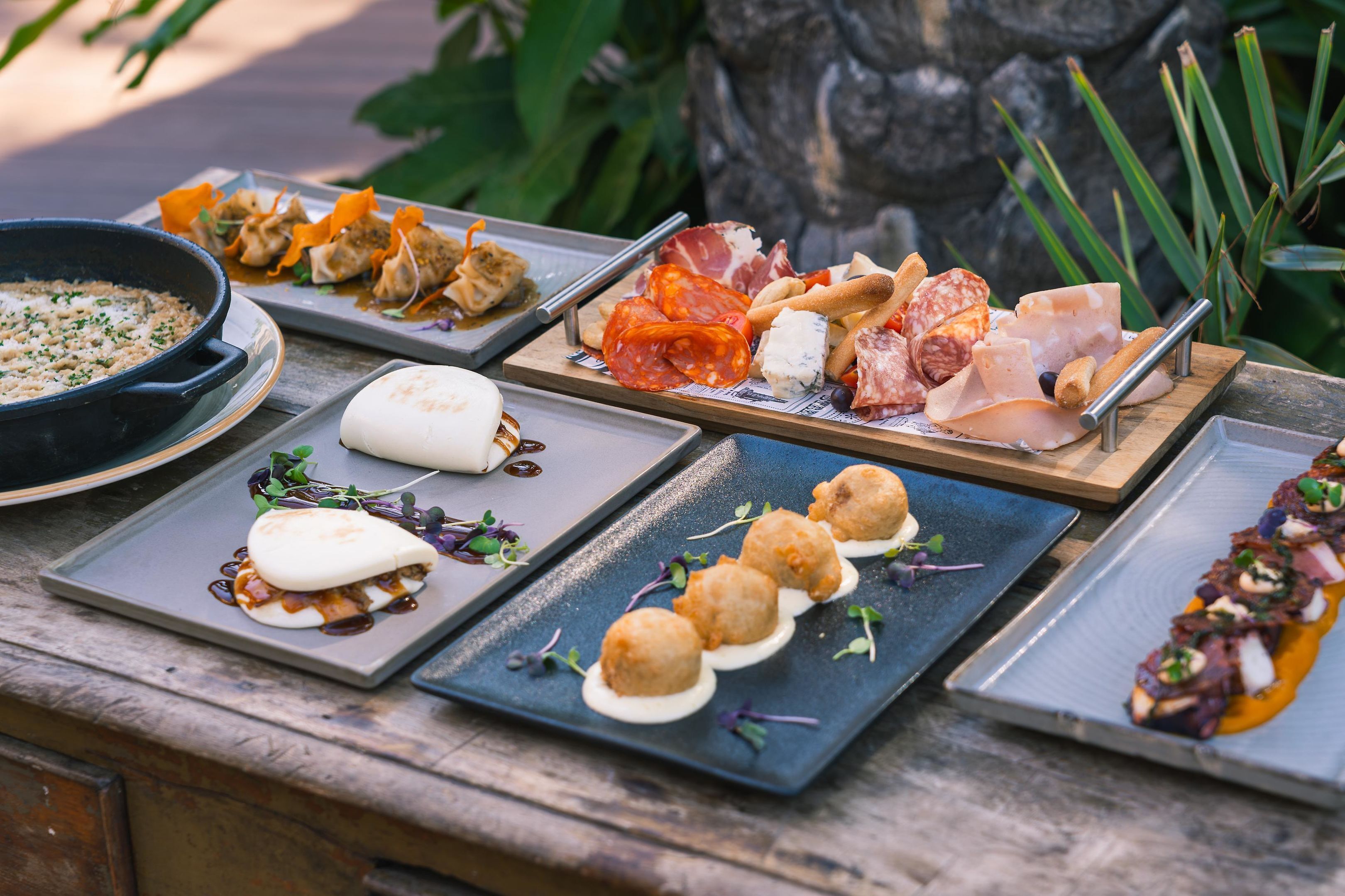 Variedad de platos sobre una mesa de madera, incluyendo un tazón de sopa, un plato de albóndigas y varias fuentes de carnes y quesos.