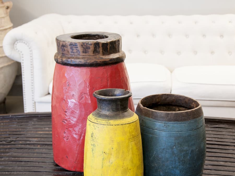 Tres macetas grandes de cerámica sobre una mesa, con un sofá blanco al fondo.