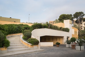 Un edificio moderno con fachada curva, una escalera que conduce a la entrada y plantas en macetas alrededor del área.