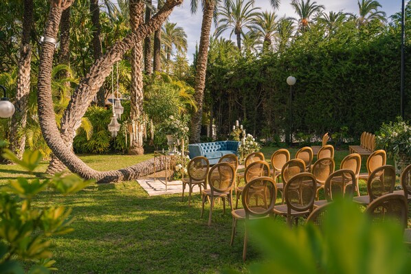 Un entorno de jardín con un sofá azul y sillas de mimbre dispuestas para un evento.