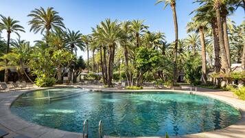 A pool surrounded by palm trees and lounge chairs.