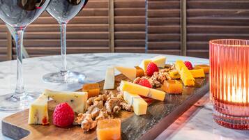 Una mesa de mármol con una tabla de madera que muestra diferentes quesos, frutas y frutos secos. Dos copas de vino tinto están colocadas a cada lado de la tabla.