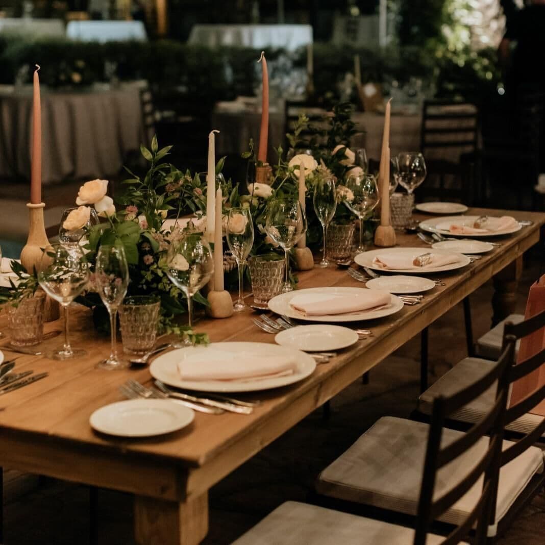 A long wooden table set for a meal with candles, glassware, and floral centerpieces.
