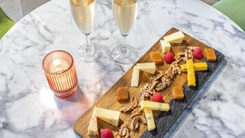 Una mesa de mármol con una tabla de madera que presenta queso, nueces y frambuesas, junto con dos copas de vino blanco y una vela encendida.