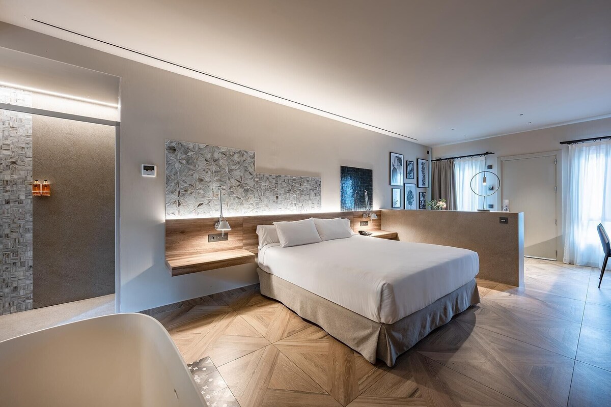 A modern hotel room with a large bed, a sitting area, and a bathroom.