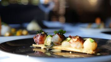 A close-up of a gourmet dish with seared scallops, a piece of bread, and a garnish.