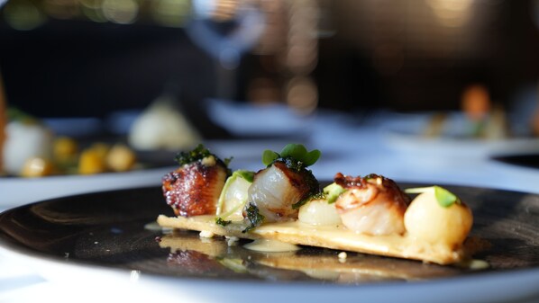 A close-up of a gourmet dish with seared scallops, a piece of bread, and a garnish. - Huerto Del Cura Hotel (Elche)