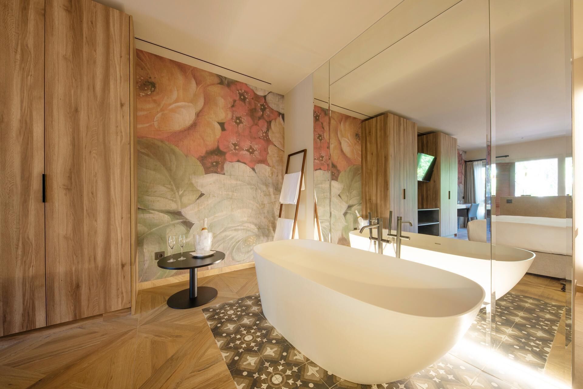 A modern bathroom with a freestanding bathtub, a round table with wine glasses, and a large mirror.