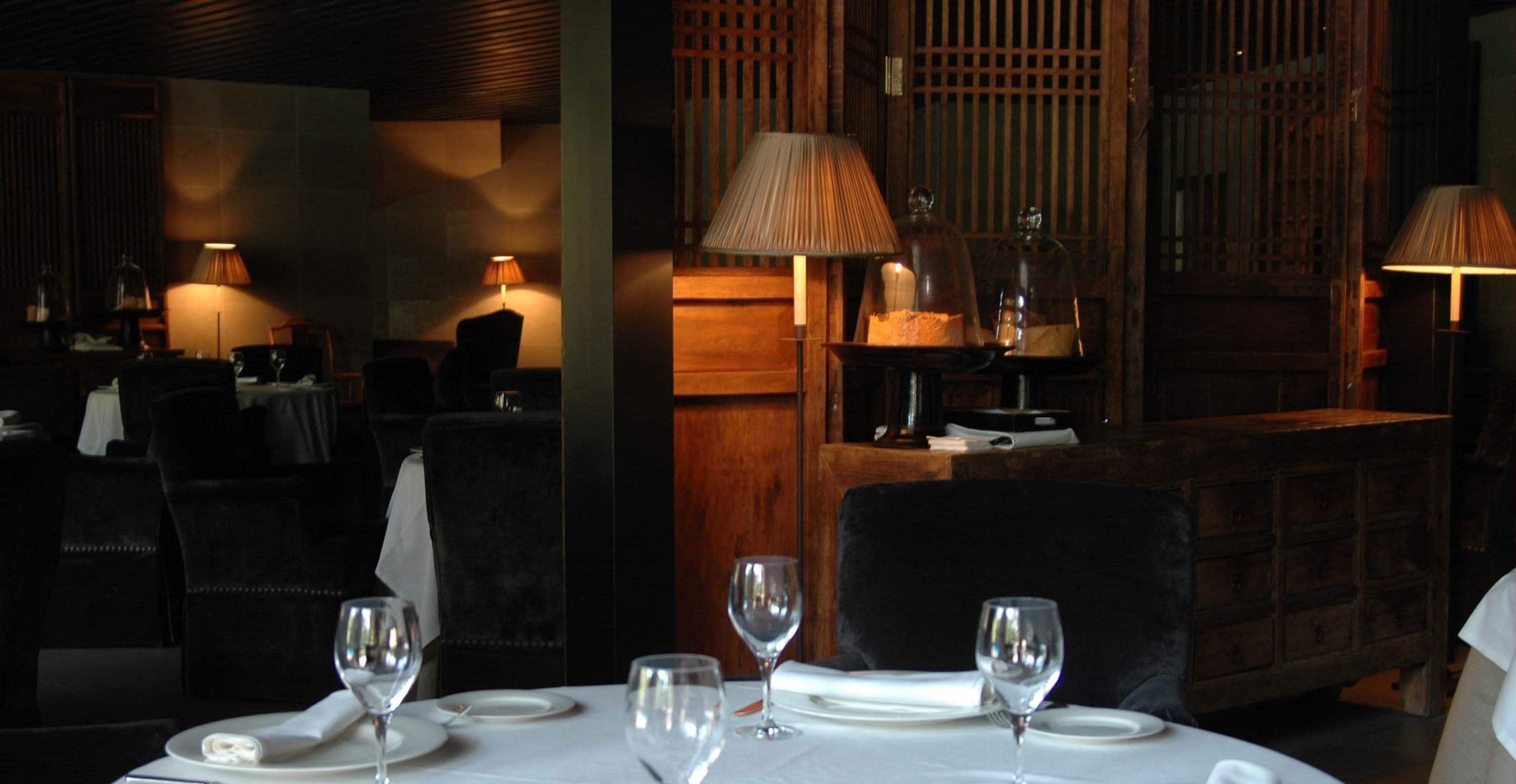Restaurante com iluminação suave, mesas preparadas para refeições, mobiliário de madeira e luzes quentes.