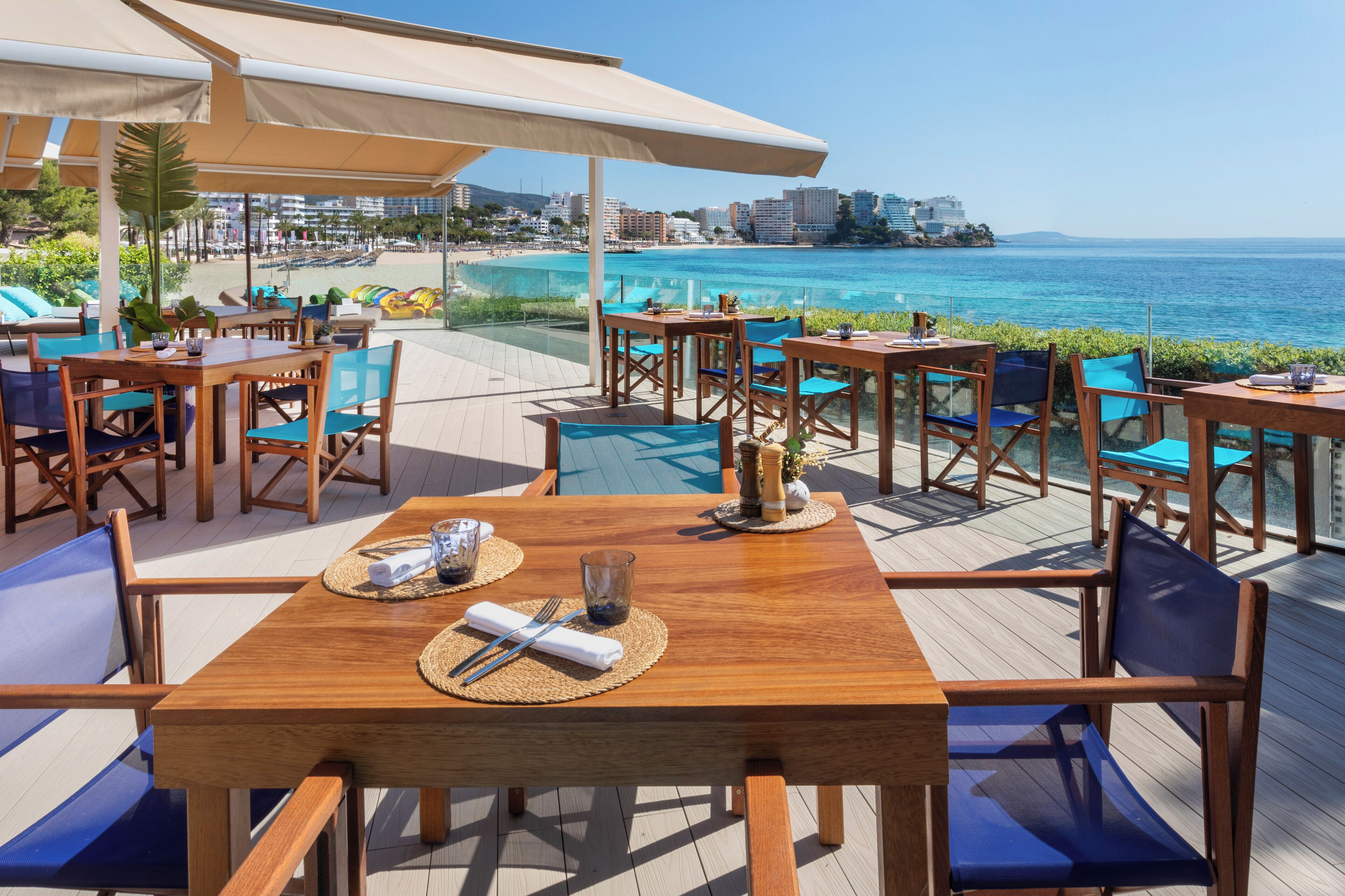 A wooden deck with tables and chairs, overlooking a beach and ocean.