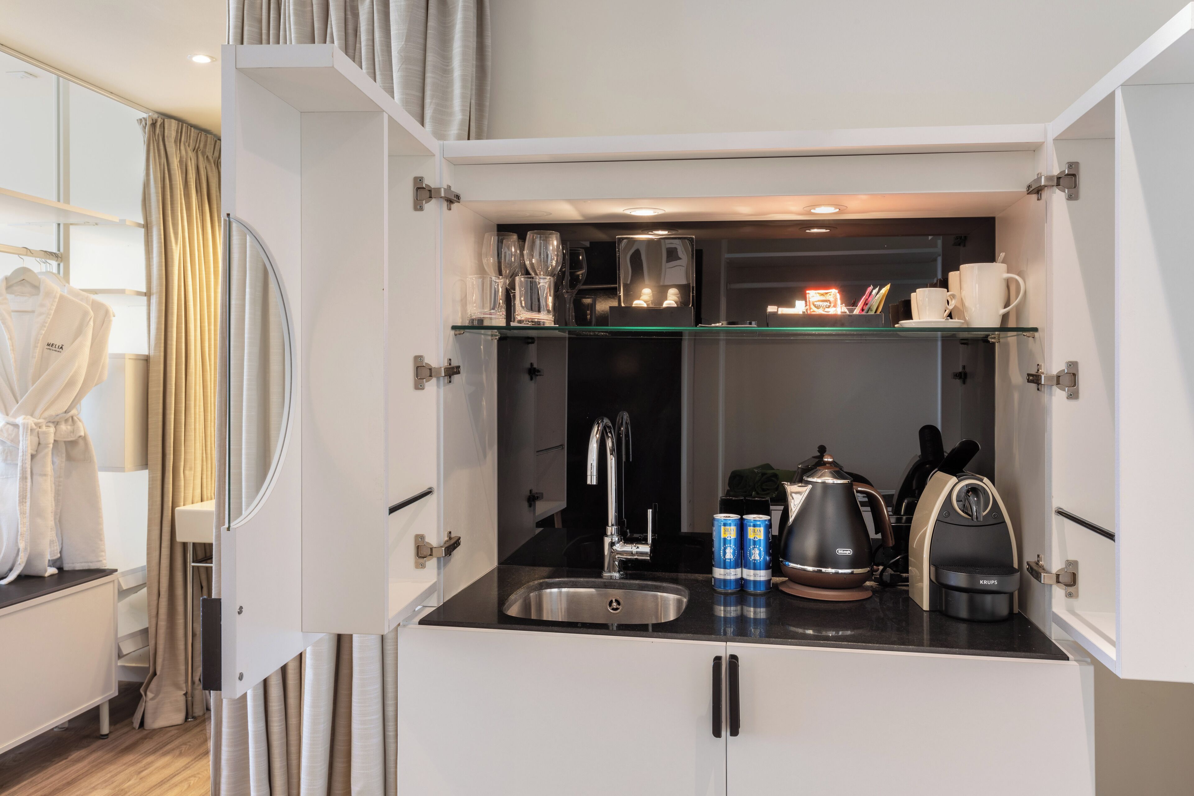 Una kitchenette compacta con un lavamanos, cafetera y estantes para guardar.