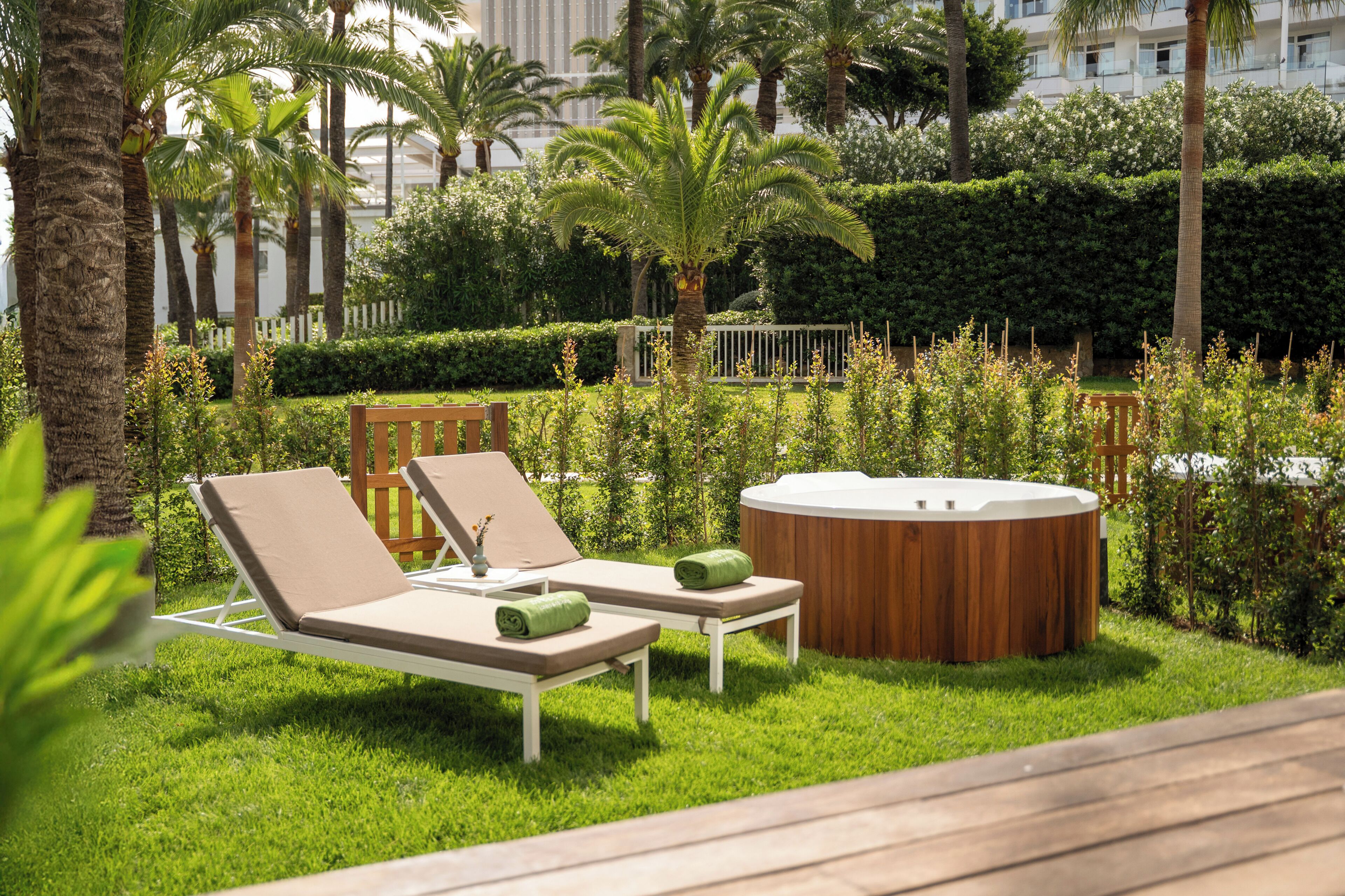 A garden area with two lounge chairs, a wooden hot tub, and a white fence.