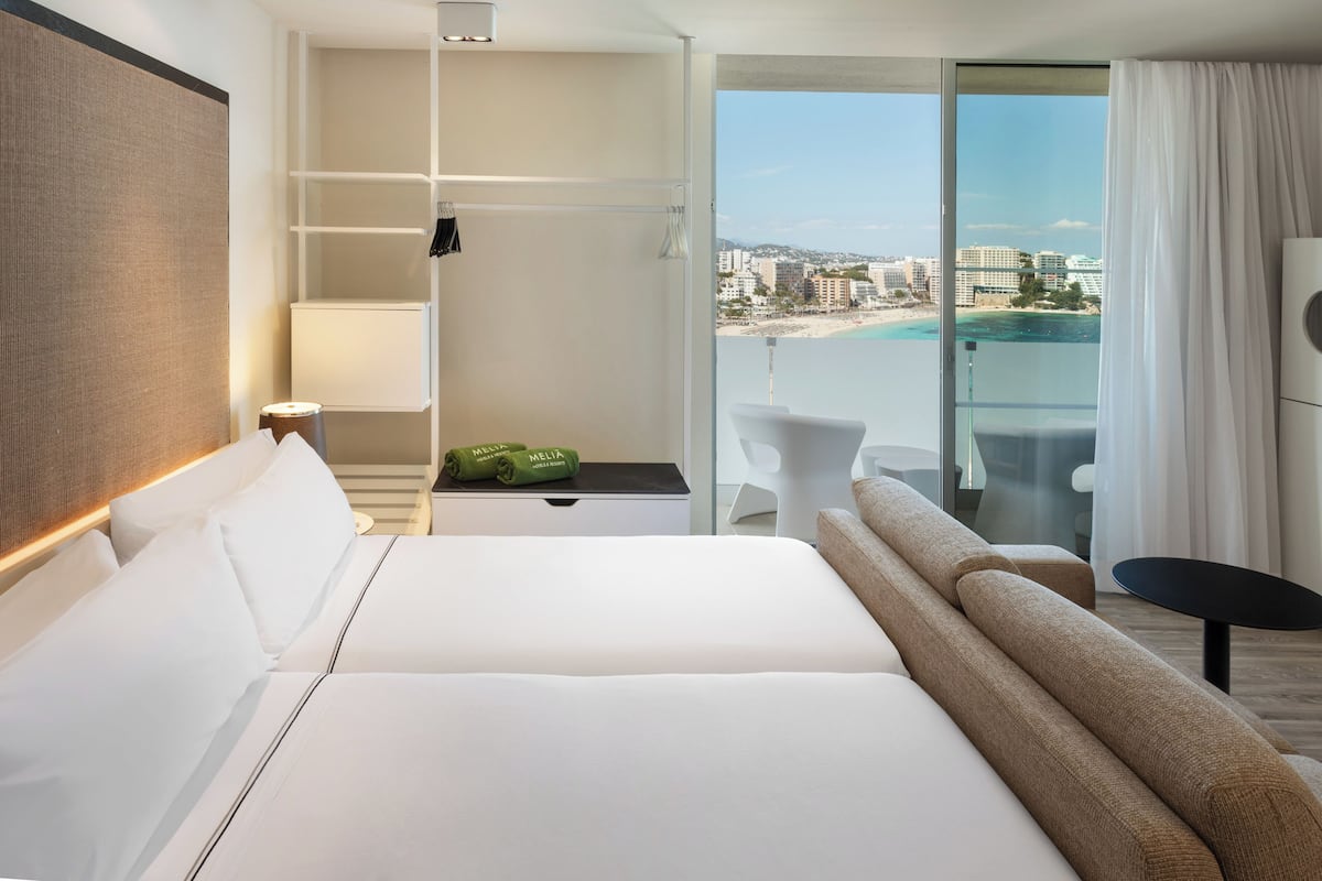 Une chambre d’hôtel avec un grand lit, un bureau, une chaise et une vue sur la plage et le paysage urbain.