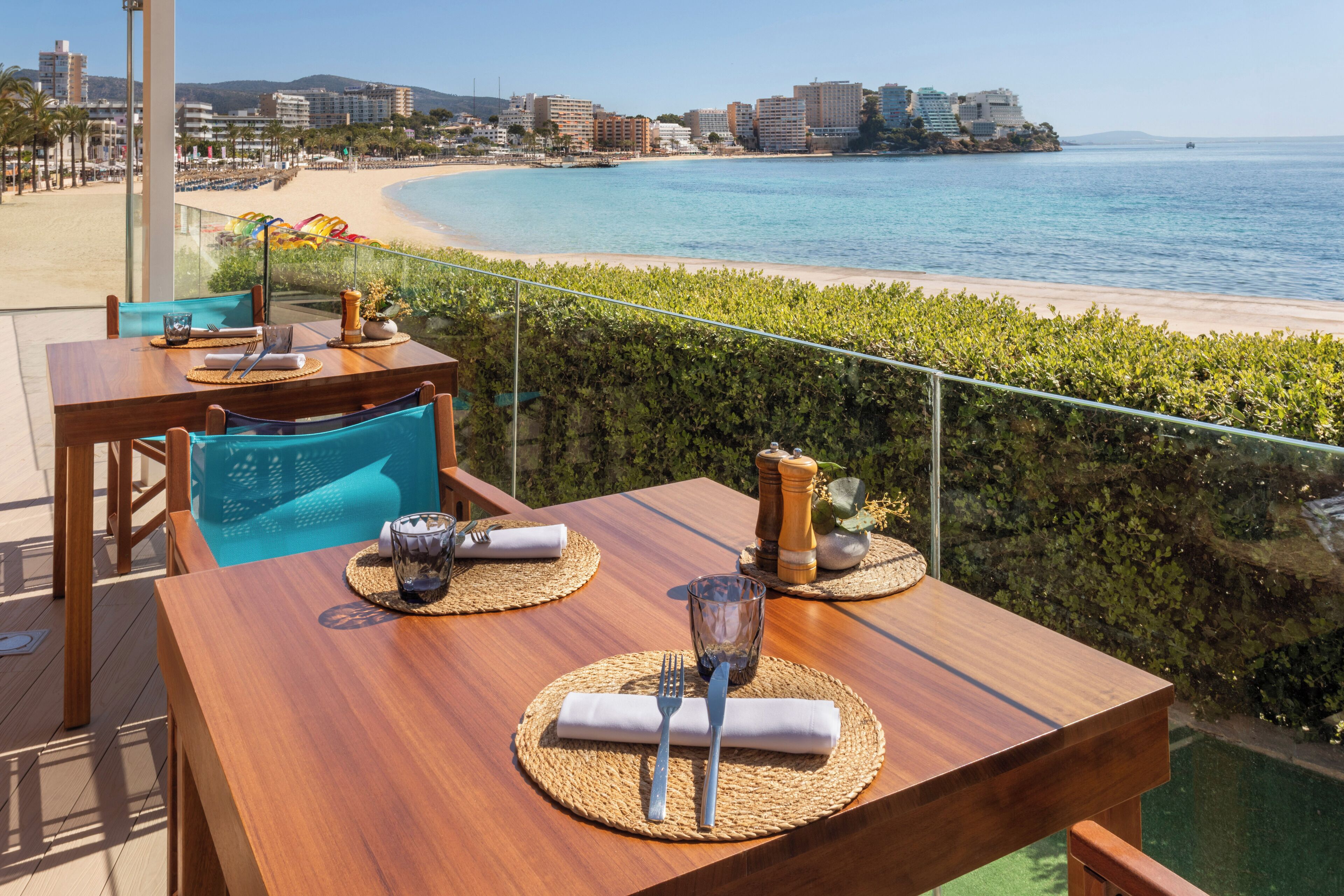 A dining table set with cutlery and napkins, overlooking a beach and ocean.