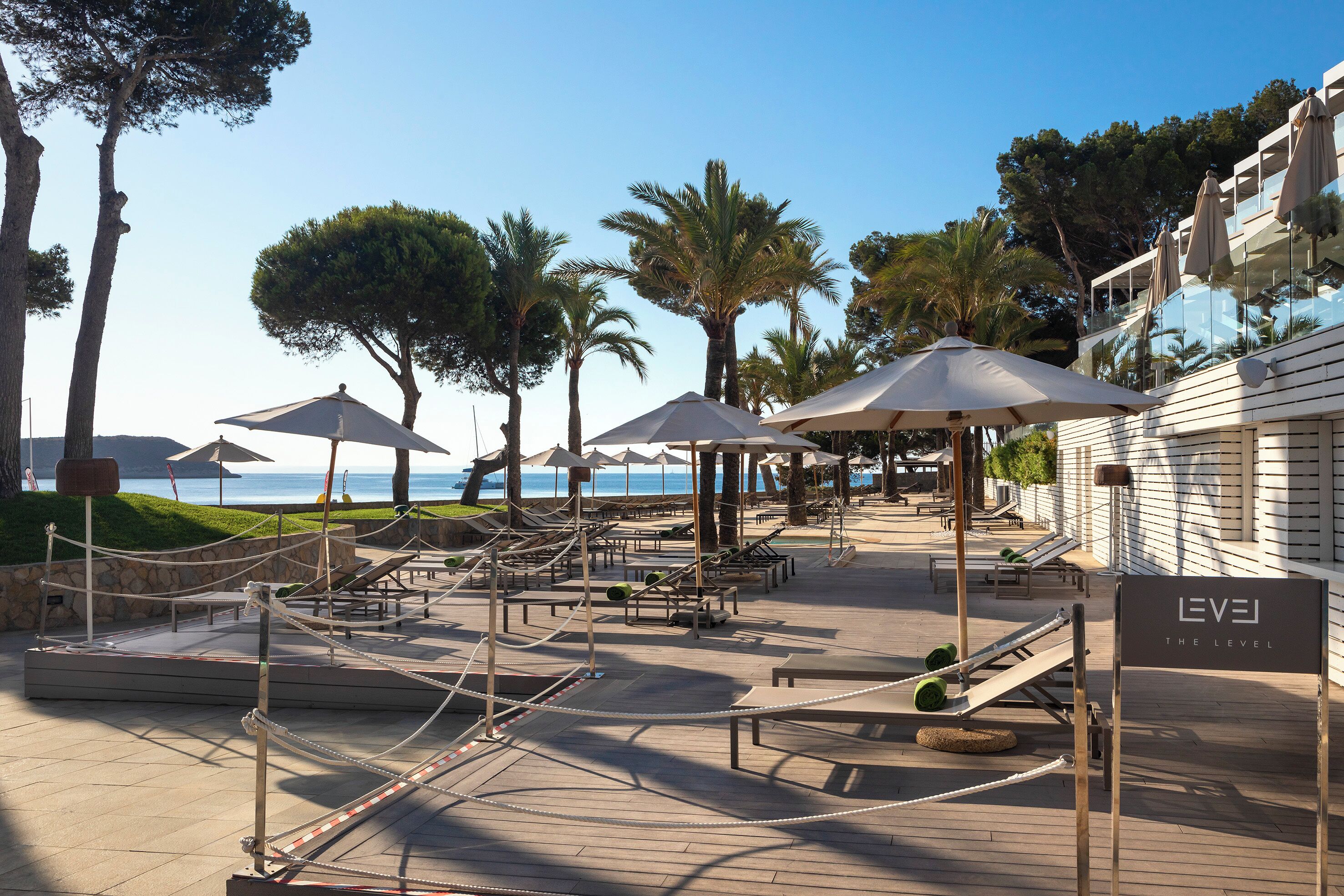 Un resort con mesas al aire libre, palmeras y vista al mar.