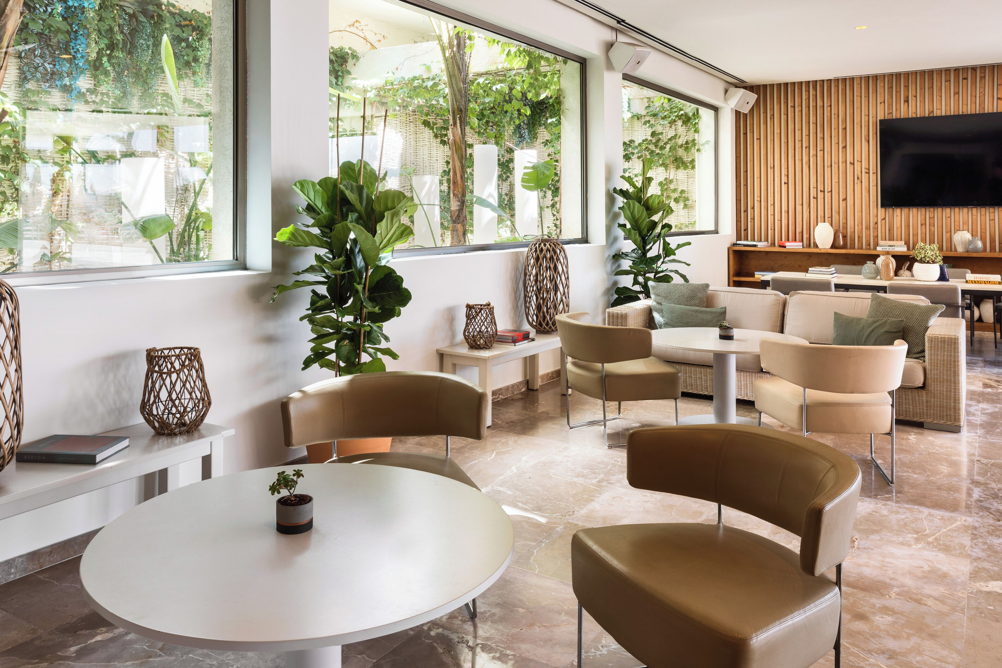 A modern living room with a round table, beige sofas, and large windows overlooking a garden.