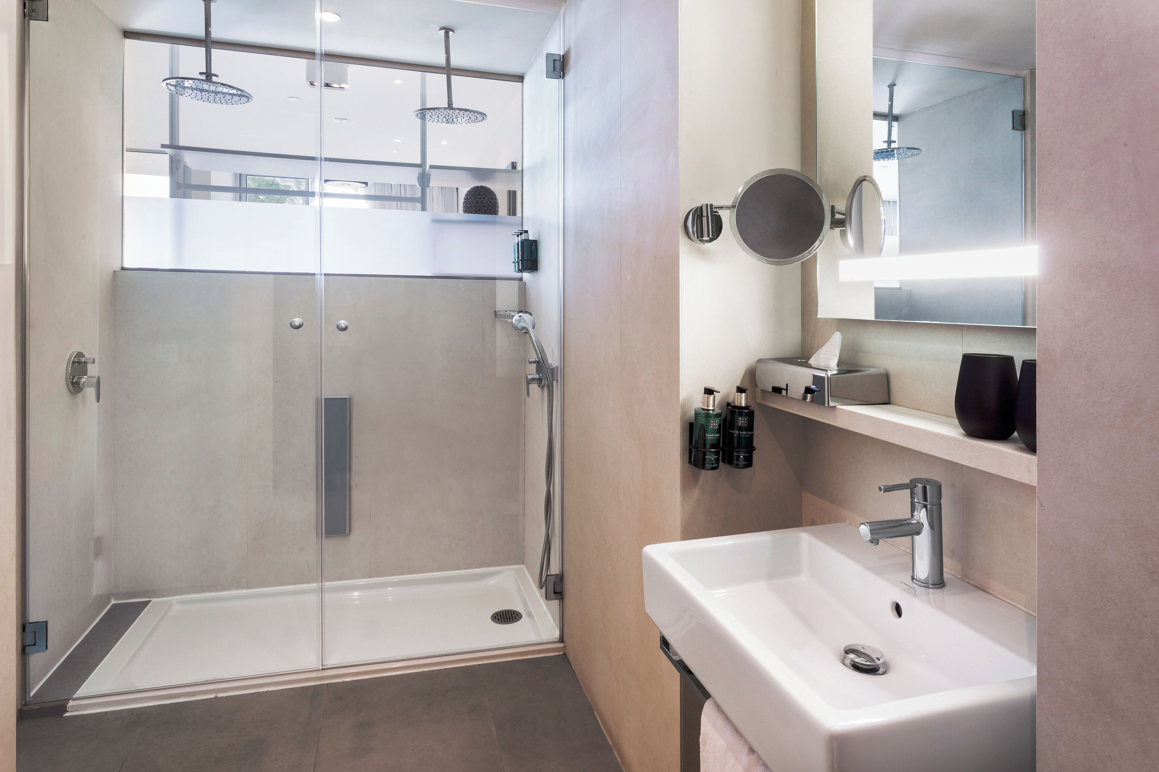 Een moderne badkamer met een douche met glazen wand, een witte wastafel en een spiegel boven de wastafel.