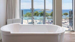 Un baño moderno con una bañera grande, ventanas amplias y vistas a una playa y al mar.
