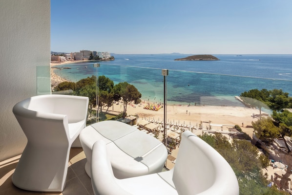 Un balcón con sillas blancas con vistas a la playa y al mar.