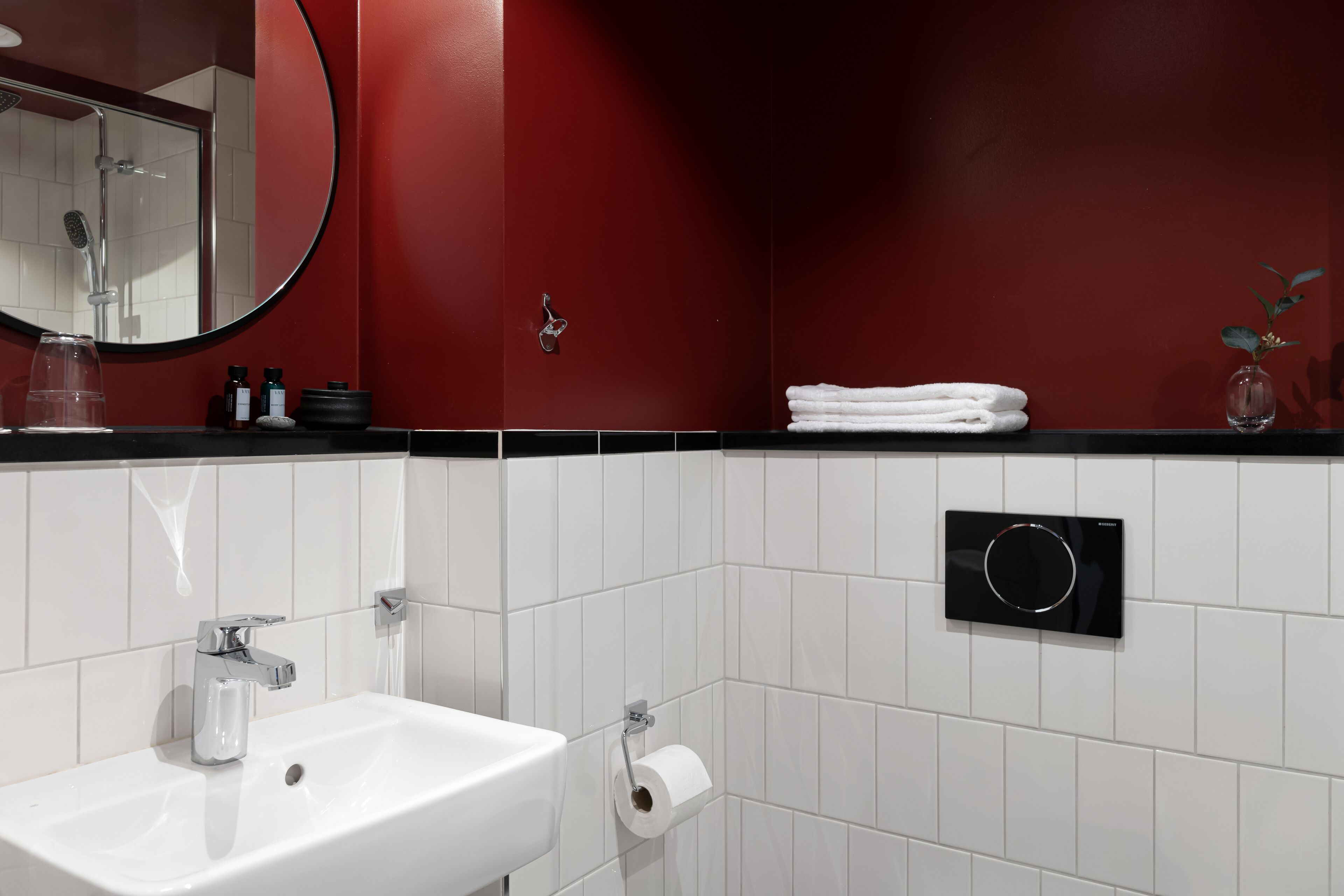 A modern bathroom with a white sink, a mirror, a towel rack, and a toilet paper holder.