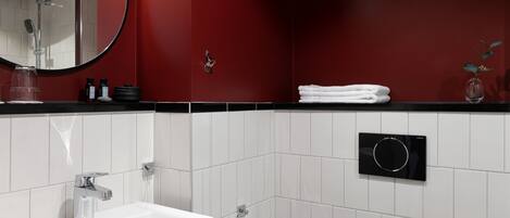 Un baño moderno con lavamanos blanco, un espejo, un perchero para toallas y un porta papel higiénico.