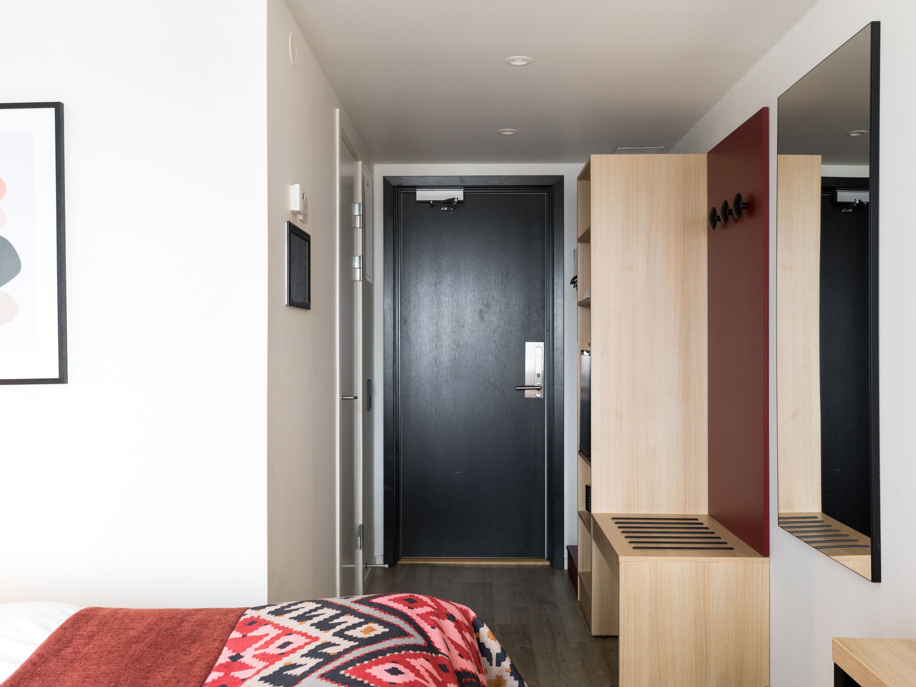 Una habitación de hotel moderna con cama, mesita de noche, espejo y armario.