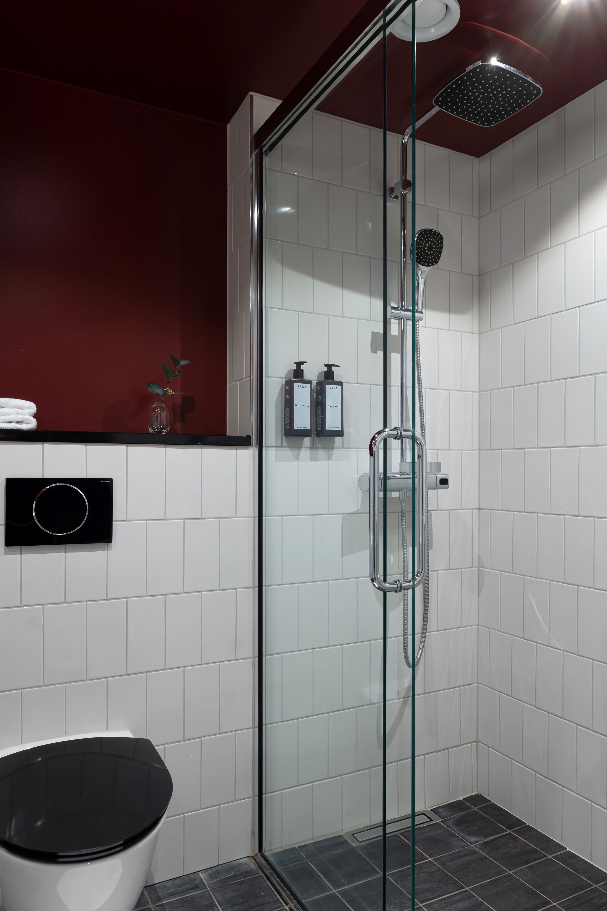 Un baño moderno con ducha de vidrio, paredes de azulejos blancos y un inodoro negro.
