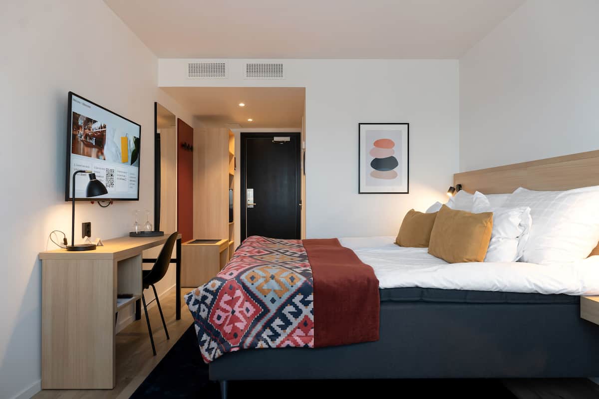 Moderni hotellihuone, jossa on sänky, työpöytä, tuoli ja seinällä oleva kehystetty taulu.