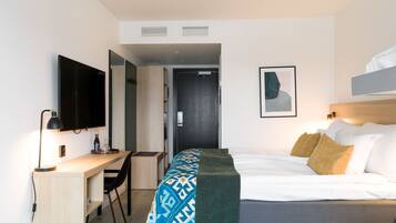 A modern hotel room with a bed, a desk, a chair, a TV, and a door.