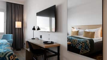 A hotel room with a bed, a desk, a chair, a lamp, and a large mirror.