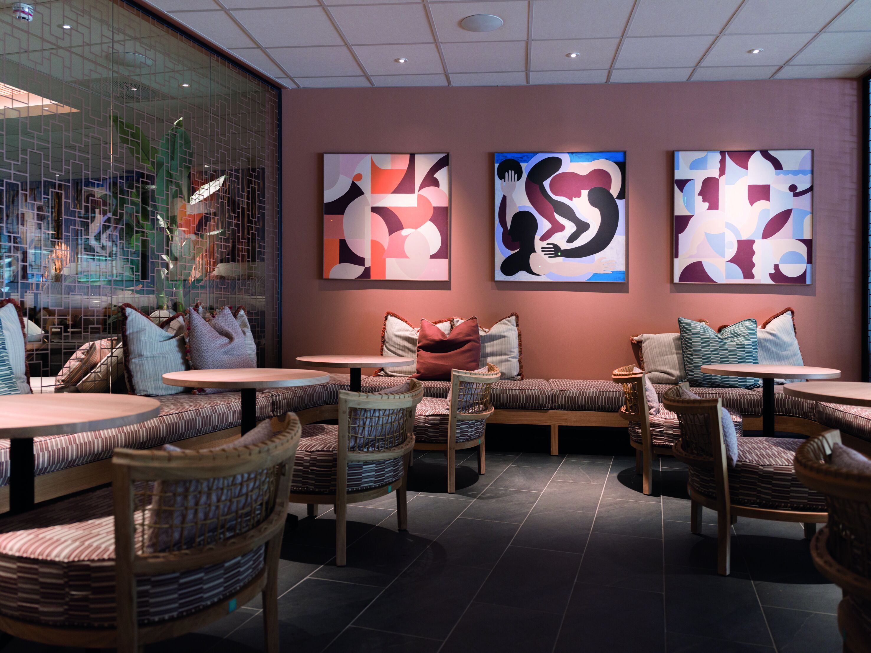 A modern lounge with cushioned seating, round tables, and abstract wall art.