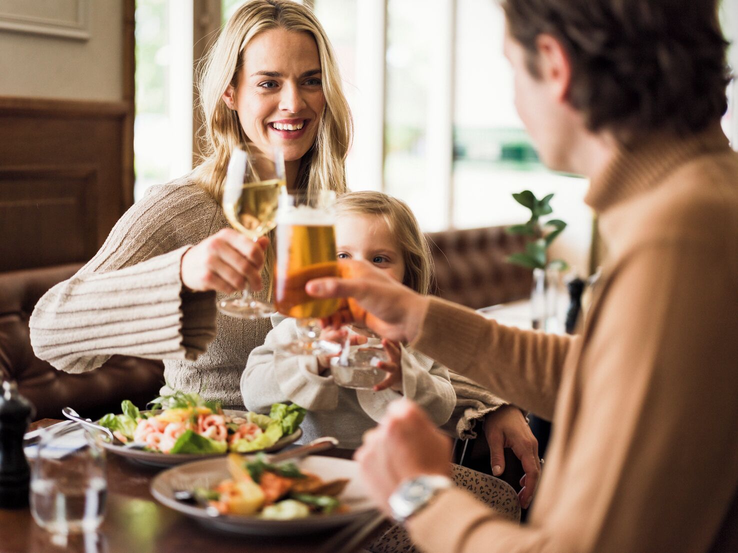 Una familia cenando en un restaurante, con una mesa lista para la comida, platos de comida y copas de vino.