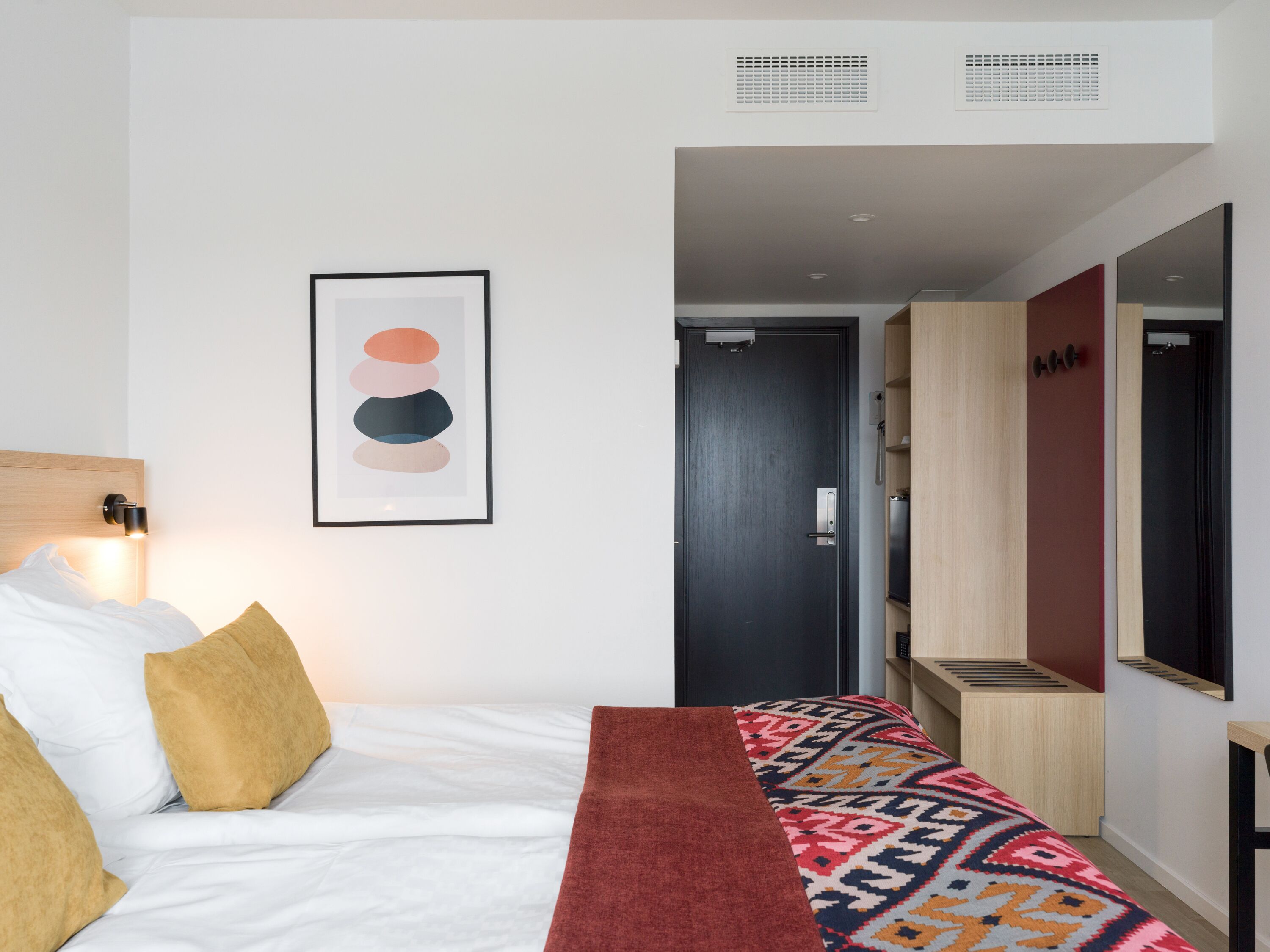 A hotel room with a bed, a framed artwork, a wardrobe, and a mirror.