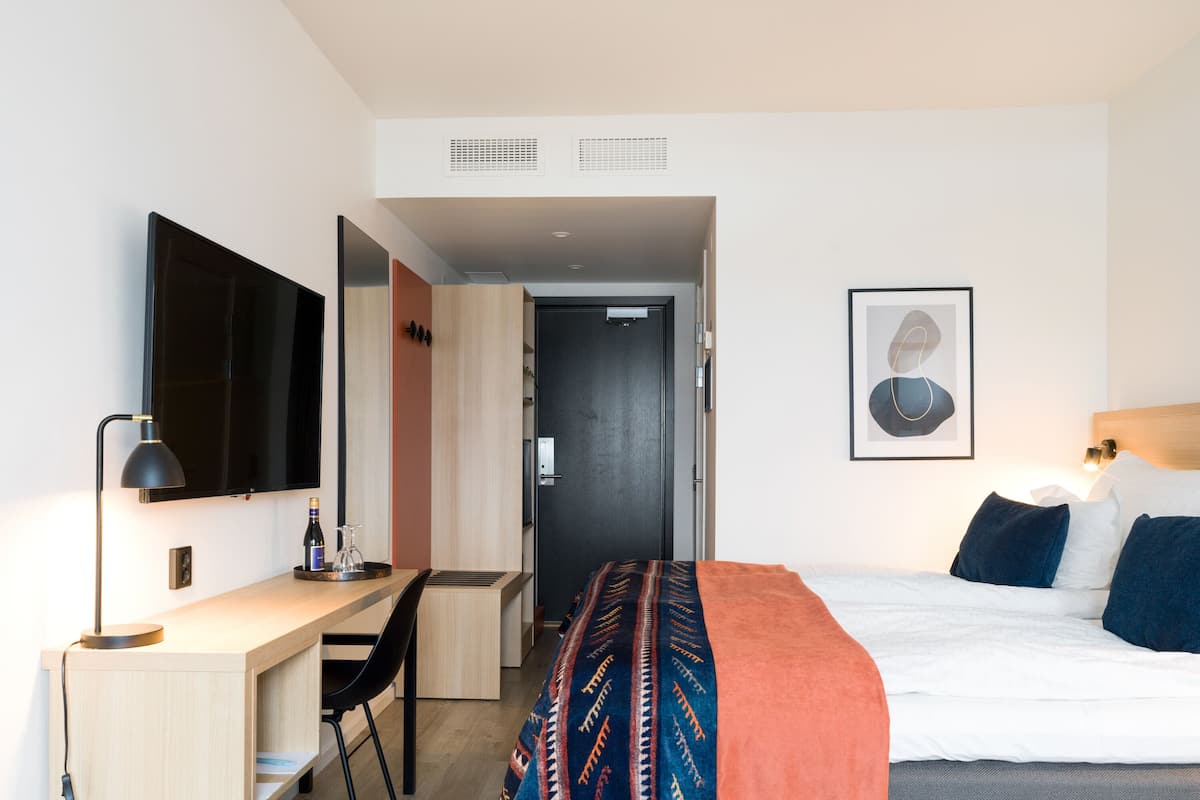Hotellihuone, jossa on sänky, työpöytä, tuoli, televisio ja ovi.