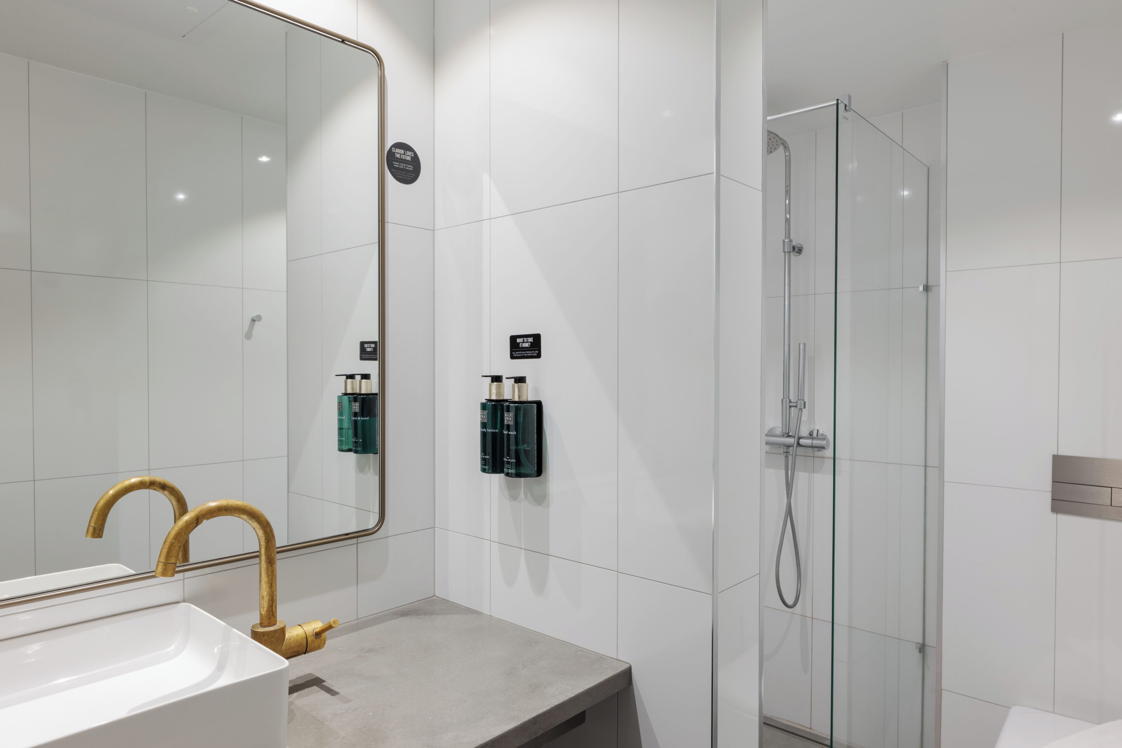 A modern bathroom with a large mirror, a sink with a gold faucet, and a glass-enclosed shower.