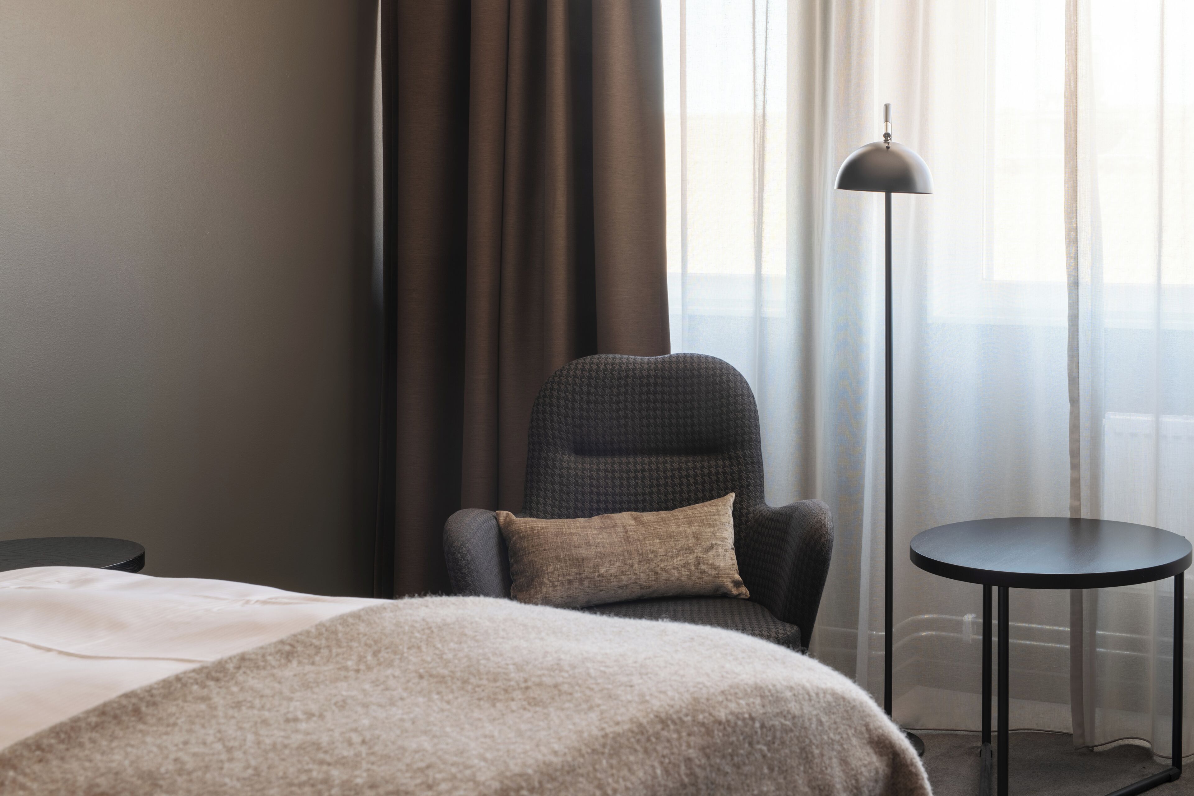 Ett hotellrum med en säng, en stol, ett litet bord och en golvlampa.