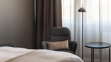 Ett hotellrum med en säng, en stol, ett litet bord och en golvlampa.