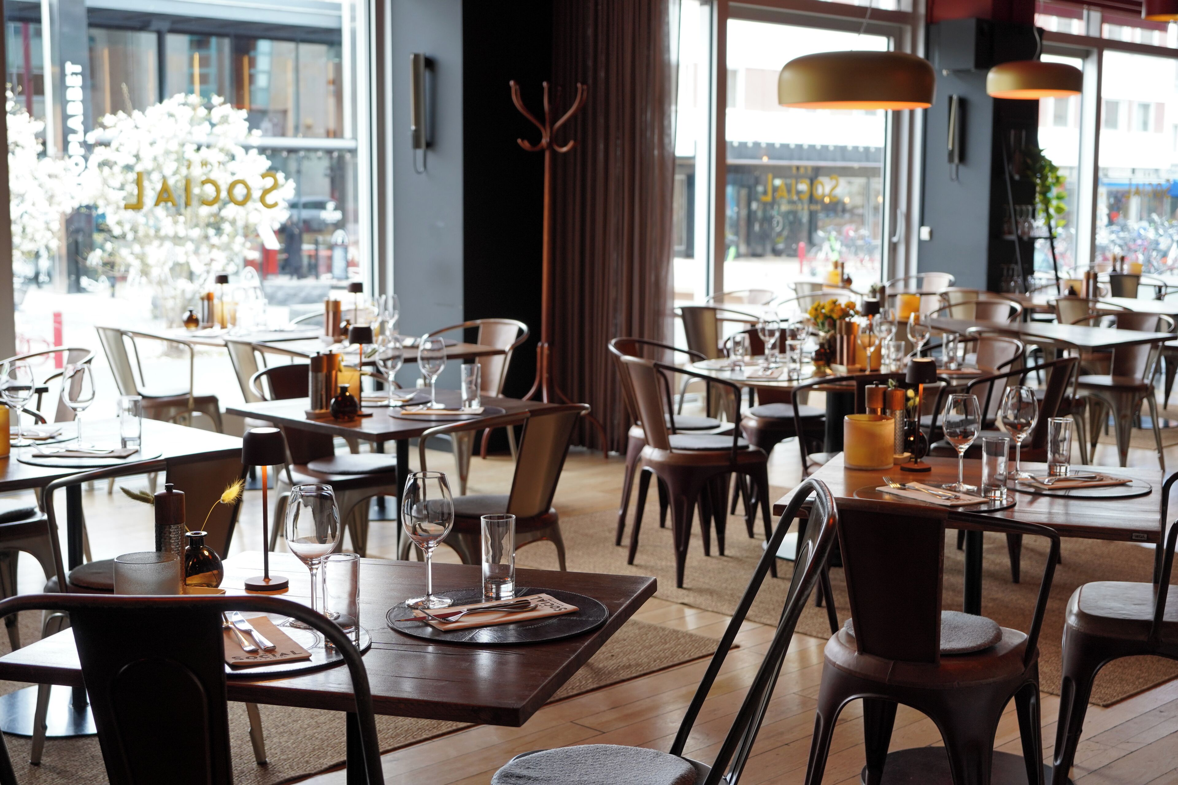 Un restaurant avec des tables dressées, des chaises et une grande fenêtre donnant sur la rue.