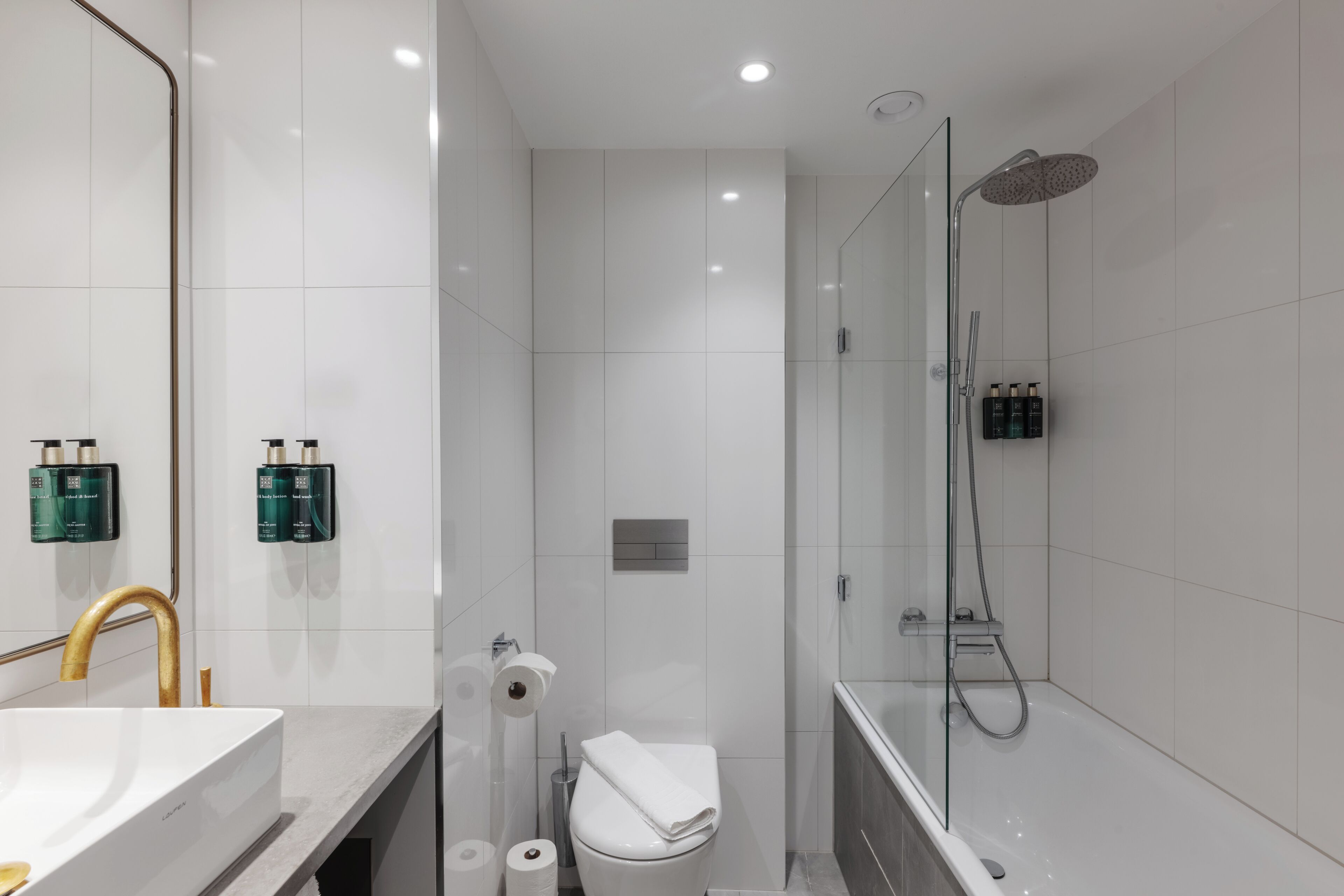 A modern bathroom with a large mirror, a white sink, a toilet, and a glass-enclosed shower area.