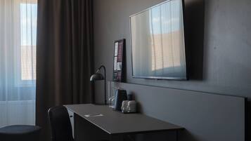 Ett hotellrum med ett skrivbord, en stol, en TV och ett fönster med gardiner.