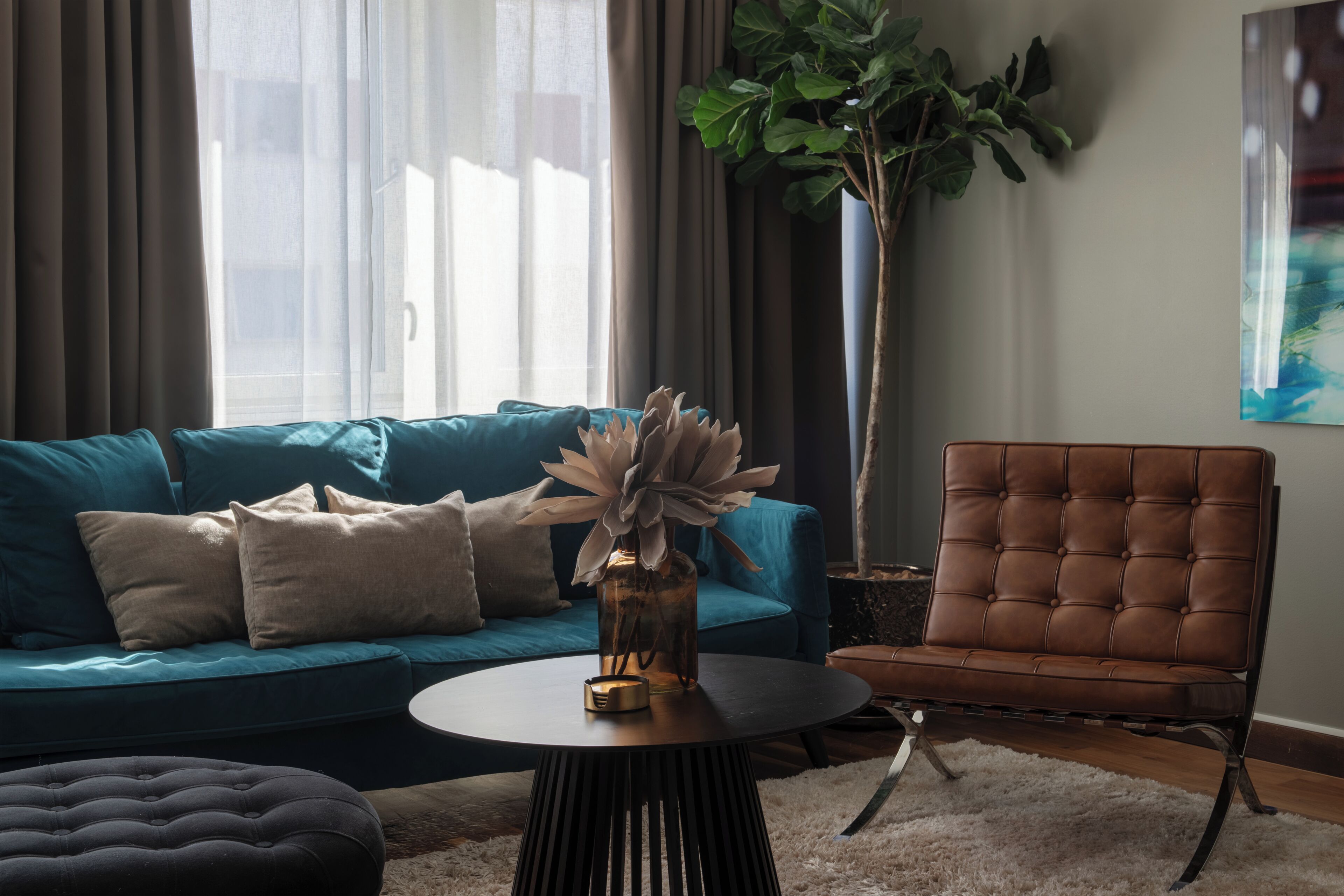 A living room with a blue sofa, a brown chair, a round coffee table, and a large plant.