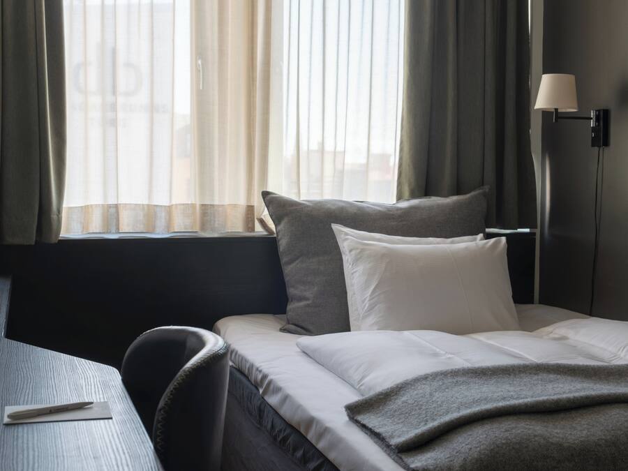 A hotel room with a bed, a desk, a lamp, and a window with curtains.