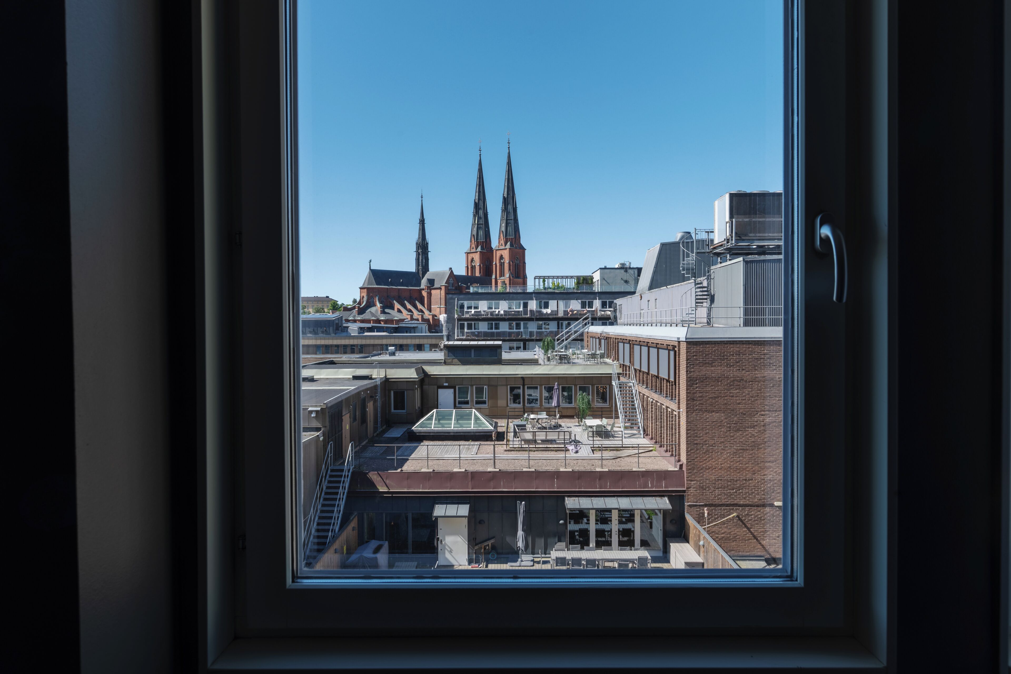 Udsigt gennem et vindue af en bygning med moderne indretning, en trappe og udsigt til en kirke med to tårne.
