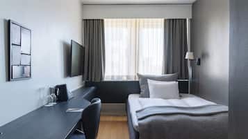 A hotel room with a bed, a desk, a chair, a TV, and a window with curtains.